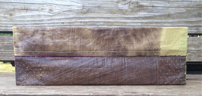 May include: A rectangular, handmade box with a two-tone design. The bottom half is a dark brown, textured material, while the top transitions from a lighter brown to a pale yellow. White stitching and a purple accent line the seam.