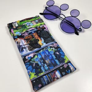 May include: A rectangular fabric glasses case featuring a colorful fantasy print with dragons, swords, and castle scenes, paired with round purple-tinted sunglasses that have small circular accents on the frames above the main lenses.