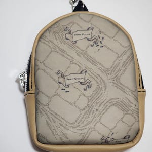 May include: A small, beige backpack-shaped coin purse with a map design. The purse has a black zipper, a silver clasp, and a black strap. The map design includes the words "Harry Potter" and "Marauders Map" on banners.