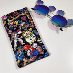 May include: A rectangular fabric glasses case featuring a black background with a colorful pattern of various video game characters including Mario, Link, and Pikachu, paired with round metal-framed sunglasses with blue-tinted reflective lenses.