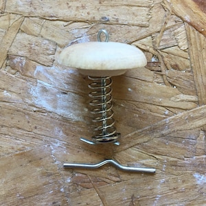May include: A wooden mushroom-shaped ornament with a metal spring and a hook. The ornament is on a brown wooden background.