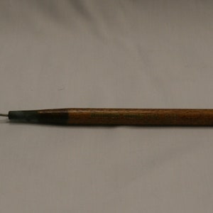 May include: A wooden-handled tool with a metal loop at one end. The handle is a light brown color, and the metal loop is attached to a dark metal section. The tool is designed for a specific purpose.