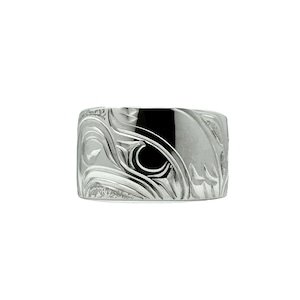 May include: A silver ring featuring an intricate carving of a stylised eagle head. The ring is wide and has a smooth, polished finish.