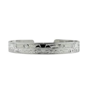 May include: A silver bracelet with a detailed design of a stylized bird or animal. The design is carved into the metal and has a raised texture.