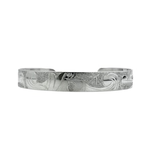 May include: A silver cuff bracelet featuring an engraved floral design. The bracelet has a textured, detailed pattern and a gently curved shape. The metal has a polished, reflective surface.