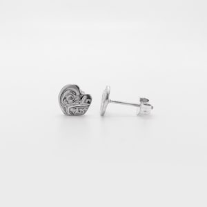 Puede incluir: Dos pendientes de plata con forma de botón. Cada pendiente presenta un diseño en forma de corazón con un patrón en relieve. Los pendientes tienen un cierre de poste y mariposa. Se muestran sobre un fondo blanco.