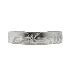 Puede incluir: Un brazalete de plata con un diseño floral grabado. El brazalete es ancho y tiene un acabado pulido. El patrón grabado cubre toda la superficie del brazalete, creando una apariencia texturizada. Mide aproximadamente 2,5 cm de ancho.