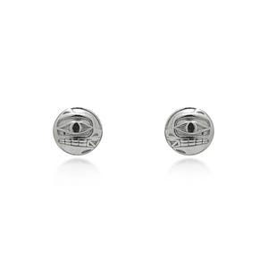 Puede incluir: Un par de pendientes de plata. Cada pendiente presenta un diseño circular con una cara grabada, que incluye un ojo y una boca. Los pendientes están sobre un fondo blanco.