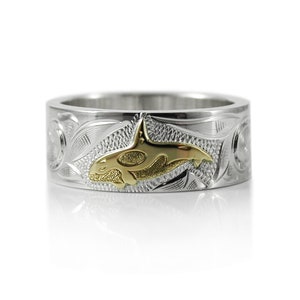 Puede incluir: Un anillo de plata con un diseño grabado y una orca dorada en el centro.