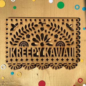 May include: A brown wooden cutout with a decorative design and the text "KREEPYKAWAII" in a stylized font.
