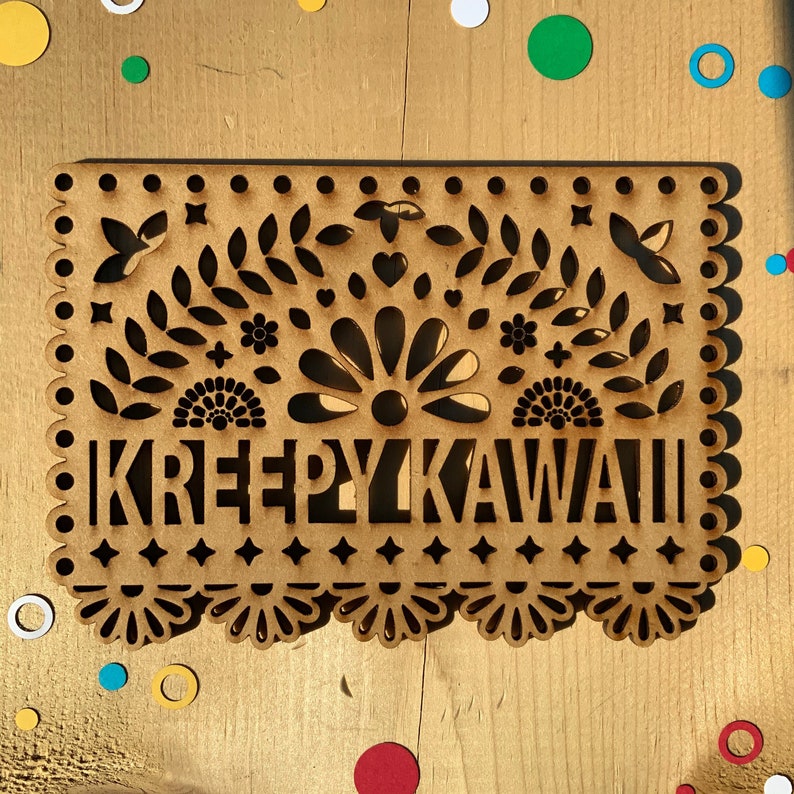 May include: A brown wooden cutout with a decorative design and the text "KREEPYKAWAII" in a stylized font.