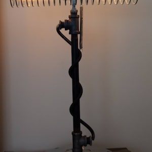 Puede incluir: Una lámpara de mesa única con una base de metal y una luminaria en forma de resorte. La lámpara está hecha de metal negro y tiene una base cromada. La luminaria está hecha de un resorte metálico en espiral con una bombilla de vidrio transparente.