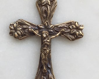 Op de afbeelding: Een gouden metalen kruis hanger met een gedetailleerd bloemmotief en een afbeelding van Jezus Christus.