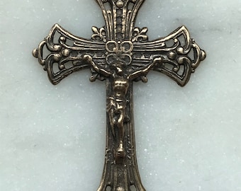 May include: A silver-toned metal crucifix pendant with an ornate design. The crucifix features a figure of Jesus Christ on the cross.