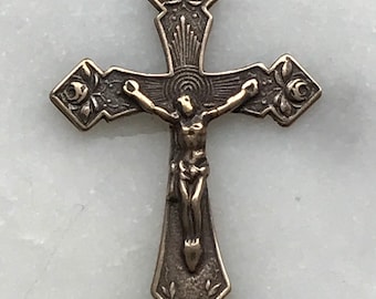 May include: A silver-toned metal crucifix with a detailed design of roses and leaves. The crucifix features a figure of Jesus Christ on the cross.