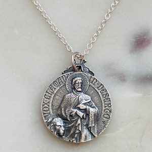 May include: Silver chain necklace with a round pendant featuring a relief image of Saint Dominic holding a book and a lily. The pendant is inscribed with "S. DOMINICUS" around the edge.