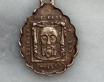 May include: A vintage, oval pendant with a scalloped edge. The pendant features an image of a bearded face within a rectangular frame, with the words "THE FACE OF THY CHRISTS" and "LOOK ON" inscribed around the image.