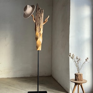 May include: A wooden hat stand with a twisted branch design and a black metal base. A beige hat is perched on the top branch.