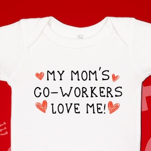 May include: White baby onesie with the text "My Mom's Go-Workers Love Me!" in black lettering and red hearts.
