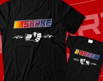 May include: Black t-shirts with the word "SHAKE" in a colorful gradient font and a fist graphic. A smaller onesie with the text "6 BAKED" and a similar fist graphic is also shown. The shirts are displayed on a red background.
