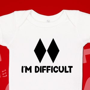 May include: White baby onesie with black diamond shapes and the text "I'm Difficult".