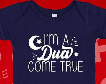May include: A navy blue baby onesie with a white crescent moon and star design. The text "I'm a Dua Come True" is printed on the onesie.