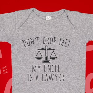 May include: Gray baby onesie with the text "Don't Drop Me! My Uncle Is A Lawyer" and a black and white illustration of a scale.