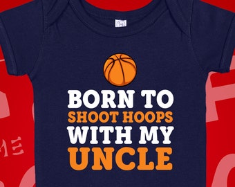 Puede incluir: Un body de bebé azul marino con una pelota de baloncesto naranja y el texto "Born to Shoot Hoops With My Uncle".