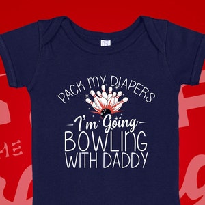 May include: A navy blue baby onesie with white text that reads "Pack my diapers - I'm going bowling with daddy". The onesie has a graphic of bowling pins and a bowling ball.