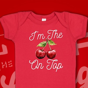 May include: Red baby onesie with white text that reads "I'm the on top" and a graphic of two red cherries with green stems and leaves.