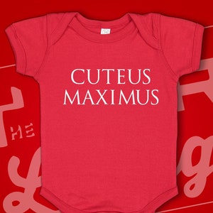 May include: Red baby onesie with white text that reads "CUTEUS MAXIMUS".