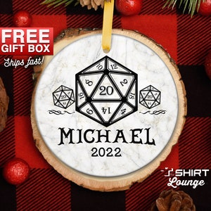 May include: A white wood round ornament with a black and white dice design. The ornament has the name "MICHAEL" and the year "2022" printed on it.