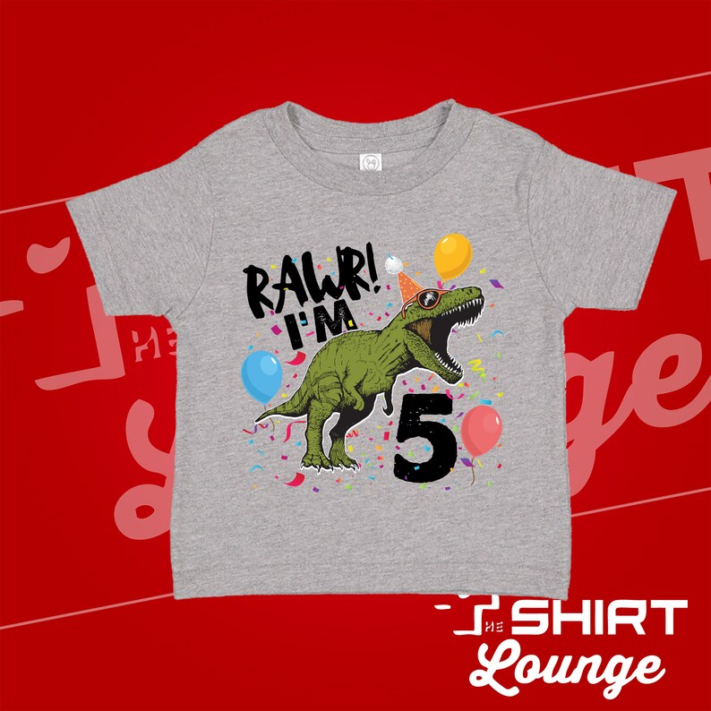 May include: Gray short-sleeved t-shirt with a green dinosaur wearing sunglasses and a party hat. The dinosaur is saying "Rawr! I'm 5" with confetti and balloons around it.