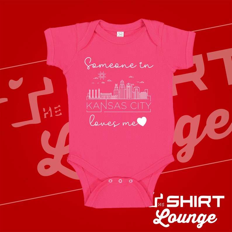 May include: Pink baby onesie with a white outline of the Kansas City skyline and the text "Someone in Kansas City loves me".