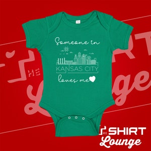 May include: Green baby onesie with a white outline of the Kansas City skyline and the text "Someone in Kansas City loves me" with a heart.