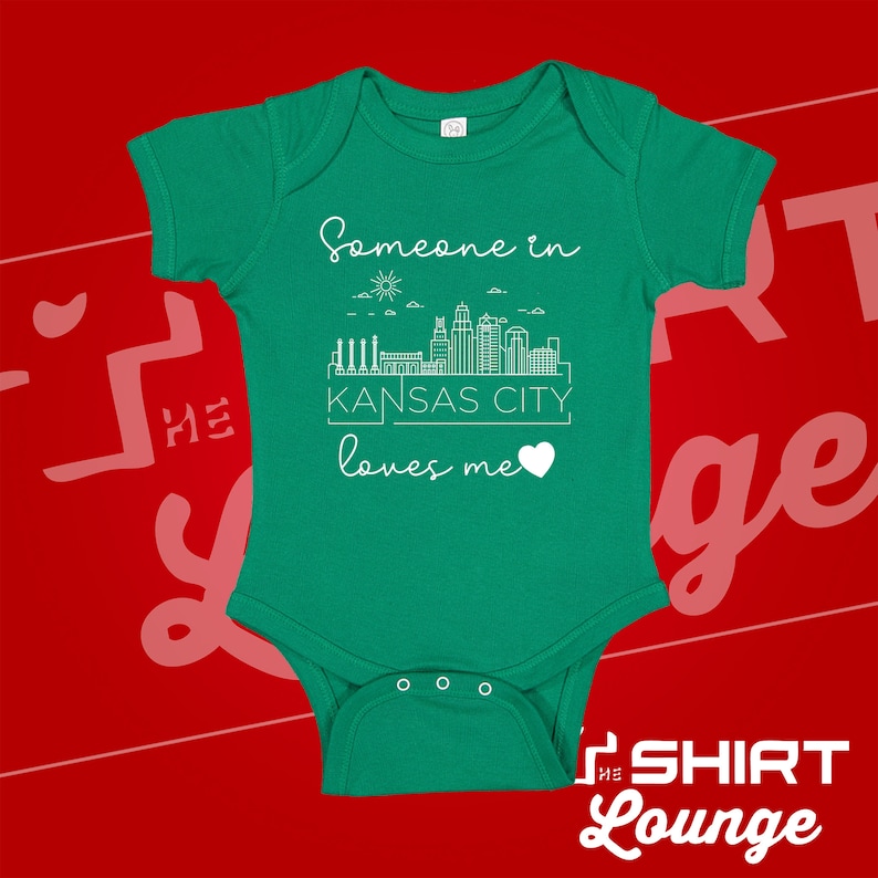 May include: Green baby onesie with a white outline of the Kansas City skyline and the text "Someone in Kansas City loves me" with a heart.