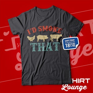 May include: A dark gray t-shirt with a vintage-style graphic that says "I'd Smoke That" and features a chicken, pig, and cow. The graphic is in red, yellow, and blue. The shirt is available in 18 colors and sizes S-4XL.