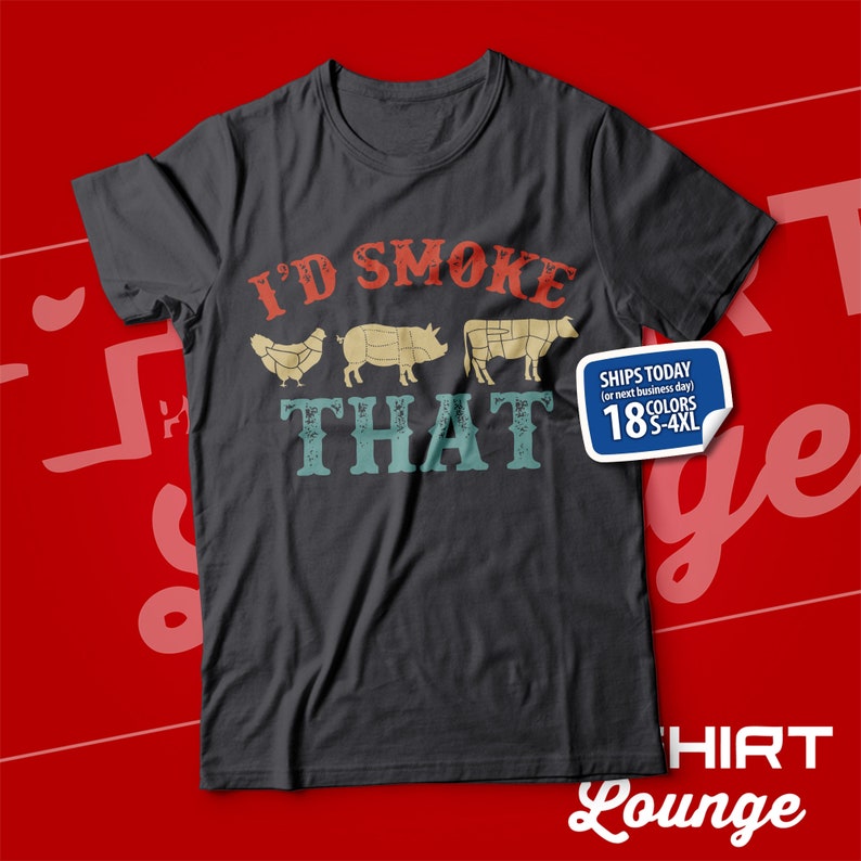 May include: A dark gray t-shirt with a vintage-style graphic that says "I'd Smoke That" and features a chicken, pig, and cow. The graphic is in red, yellow, and blue. The shirt is available in 18 colors and sizes S-4XL.
