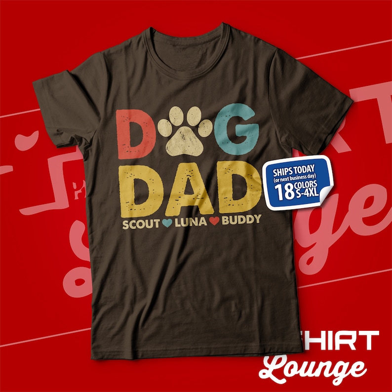 May include: A brown t-shirt with the text "Dog Dad" in a retro style with a paw print in the middle of the "O". The text "Scout Luna Buddy" is below the main text with a heart between each name.