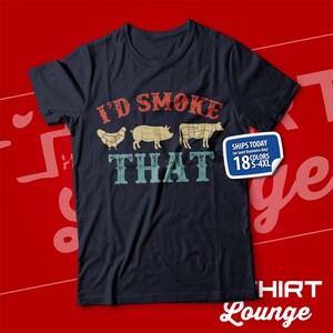 May include: A dark blue t-shirt with the text "I'd Smoke That" in a vintage style font. The text is surrounded by images of a chicken, pig, and cow. The shirt is available in 18 colors and sizes S-4XL.