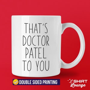 Pode incluir: Caneca de cer&acirc;mica branca com texto preto que diz "That's Doctor Patel to you". A caneca tem uma al&ccedil;a e &eacute; impressa em ambos os lados.