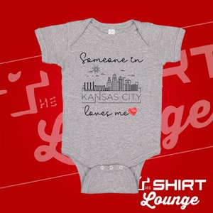 May include: Gray baby onesie with a black graphic of a city skyline and the text "Someone in Kansas City loves me" with a red heart.