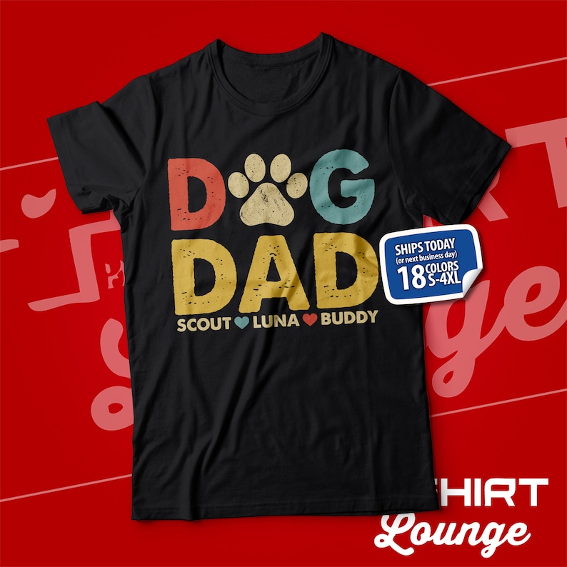 May include: Black t-shirt with a vintage-style graphic that says "Dog Dad" with a paw print in the "O". The graphic is in red, yellow, and blue. Below the graphic, it says "Scout Luna Buddy" with a red heart between each name.