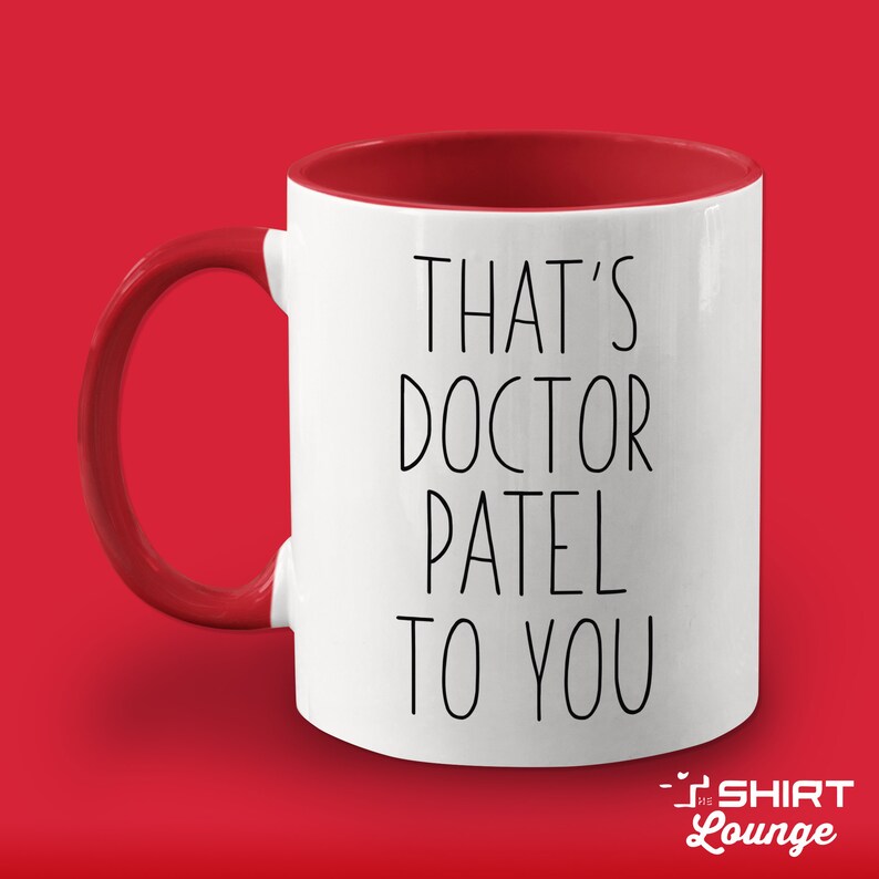 Pode incluir: Caneca de cer&acirc;mica branca com borda e al&ccedil;a vermelhas. A caneca tem texto preto que diz "That's Doctor Patel to you".