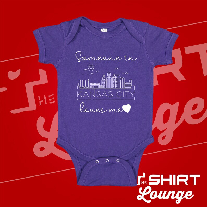 May include: Purple baby onesie with a white outline of the Kansas City skyline and the text "Someone in Kansas City loves me" with a heart.