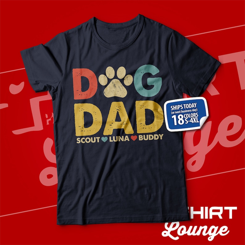 May include: A navy blue t-shirt with a vintage-style graphic that says "Dog Dad" with a paw print in the "O". The graphic is in red, yellow, green, and blue. Below the graphic, it says "Scout Luna Buddy" with a red heart between each name.