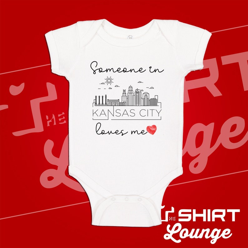 May include: White baby onesie with a black outline of the Kansas City skyline and the text "Someone in Kansas City loves me" with a red heart.