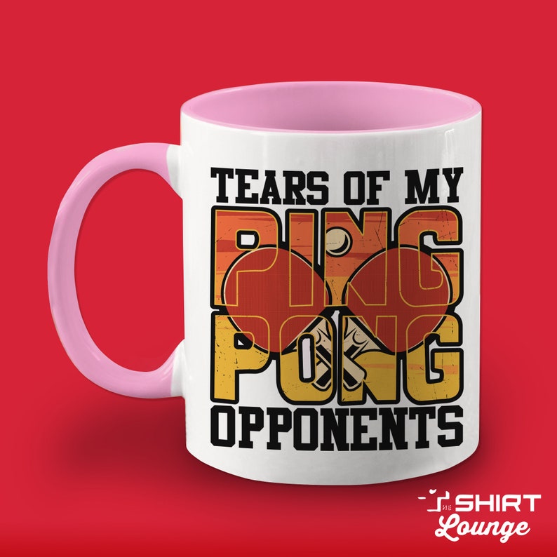 May include: White ceramic coffee mug with a pink handle. The mug has a vintage-style graphic of a ping pong paddle and ball with the text "Tears of my Ping Pong Opponents".