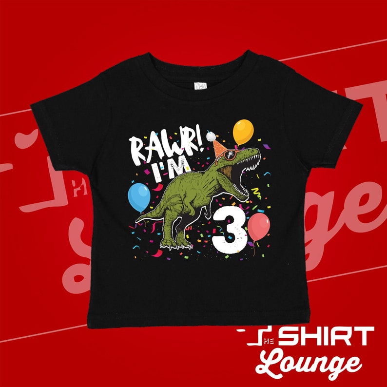 May include: Black t-shirt with a green dinosaur wearing a party hat and sunglasses. The dinosaur is surrounded by confetti and balloons. The text "Rawr! I'm 3" is printed on the shirt.