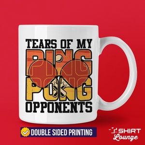 May include: White ceramic coffee mug with a vintage-style design featuring the text "Tears of my Ping Pong Opponents". The design includes two red and orange ping pong paddles with a white ball. The text is in black and the background is a faded orange and yellow.